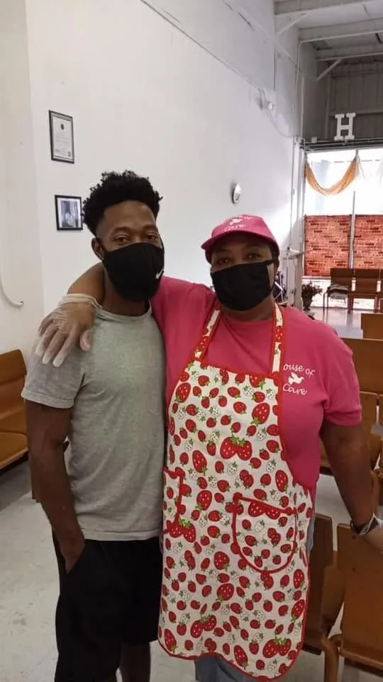 Two House of Care volunteers in the fellowship hall, one in a House of Care apron